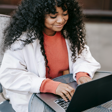 Woman in white jacket using a laptop outdoors with a smile